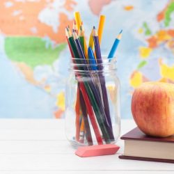 Colored Pencils In Mason Jar Next To Books C Eraser C And An Apple On Top Of A Book